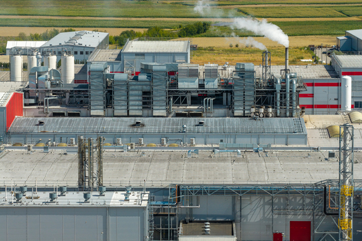 Aerial view of an advanced ventilation system on the roof of a large food factory with smoke rising from a chimney and surrounding agricultural fields in Poland.