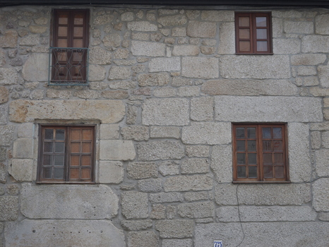 View of a traditional stone wall with three wooden framed windows in the historic center of Covilha Castelo Branco District Portugal.