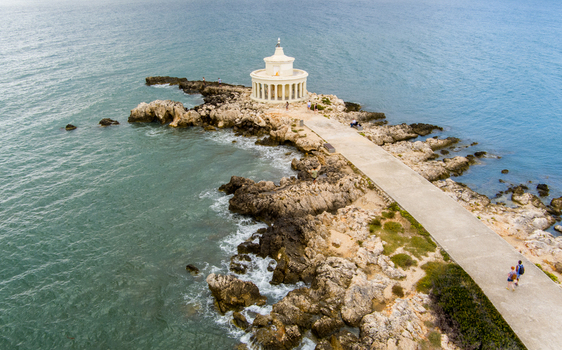Aerial view of the Saint Theodore Lighthouse situated on a rocky peninsula with a concrete walkway and turquoise sea in Argostoli Greece.