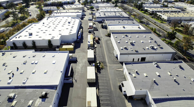 Aerial view of manufacturing buildings and warehouses with flat roofs parking lots and shipping containers in an industrial park in Los Angeles California United States.