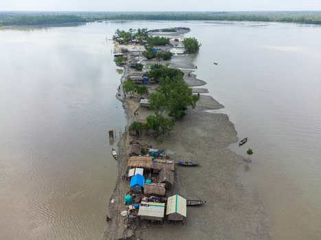 Aerial view of Kalabagi village on a narrow strip of land with small huts lush trees and wooden boats along the muddy riverbanks Khulna District Khulna Division Bangladesh.
