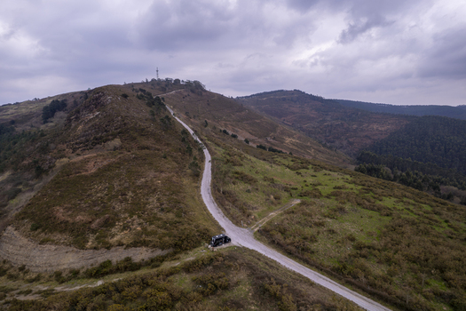 Aerial view of a camper van parked on a winding dirt road traversing the rolling green hills of the Basque countryside in Gaztelugatxeko Doniene Euskadi Spain. Aerial view of a camper van parked on a winding dirt road traversing the rolling green hills of the Basque countryside in Gaztelugatxeko Doniene Euskadi Spain.