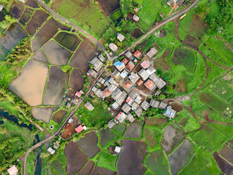 Aerial view of a small village nestled within the lush green landscape of the Sahyadri Mountains surrounded by flooded rice paddies and agricultural fields in Pune Maharashtra India. Aerial view of a small village nestled within the lush green landscape of the Sahyadri Mountains surrounded by flooded rice paddies and agricultural fields in Pune Maharashtra India.