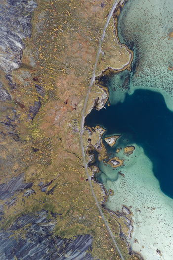 Aerial view of the Lofoten landscape featuring a winding coastal road rocky terrain and turquoise waters of the Norwegian Sea in Leknes Nordland Norway. Aerial view of the Lofoten landscape featuring a winding coastal road rocky terrain and turquoise waters of the Norwegian Sea in Leknes Nordland Norway.