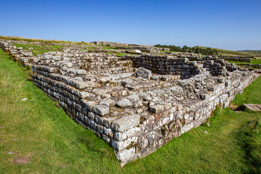 View of the ancient Roman ruins of Vindolanda featuring stone walls and foundations under a clear blue sky Hexham England United Kingdom. View of the ancient Roman ruins of Vindolanda featuring stone walls and foundations under a clear blue sky Hexham England United Kingdom.
