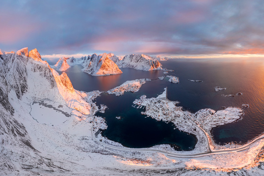Aerial view of the snow covered mountains and coastal villages of the Lofoten islands under a colorful sunset sky in Nordland Norway.