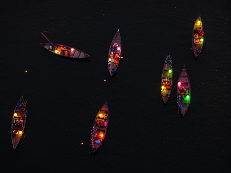 Aerial view of small wooden boats illuminated by colorful lanterns floating on dark water at night with people on board in Vietnam. Aerial view of small wooden boats illuminated by colorful lanterns floating on dark water at night with people on board in Vietnam.