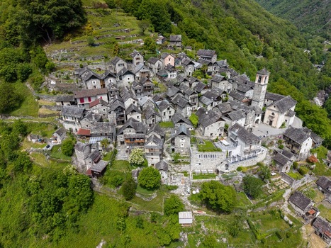 Aerial view of the historic stone houses of Corippo Albergo Diffuso nestled on a lush green hillside with traditional slate roofs and a church tower in Corippo Ticino Switzerland. Aerial view of the historic stone houses of Corippo Albergo Diffuso nestled on a lush green hillside with traditional slate roofs and a church tower in Corippo Ticino Switzerland.