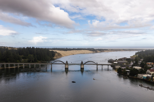 Aerial view of Siuslaw River Bridge spanning the Siuslaw River with sand dunes dense forest and small fishing boats in the water in Florence Oregon United States. Aerial view of Siuslaw River Bridge spanning the Siuslaw River with sand dunes dense forest and small fishing boats in the water in Florence Oregon United States.