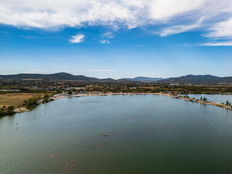 Aerial view of Lake Lupa s broad water beach facilities and green shoreline with Budakalasz and low hills beyond in Hungary under a cloud streaked summer sky.