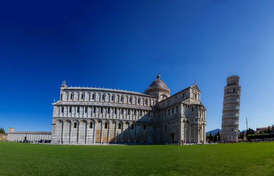 View of the Leaning Tower of Pisa and the Cathedral of Pisa standing on the green lawn of the Piazza dei Miracoli under a clear blue sky in Pisa Toscana Italy. View of the Leaning Tower of Pisa and the Cathedral of Pisa standing on the green lawn of the Piazza dei Miracoli under a clear blue sky in Pisa Toscana Italy.