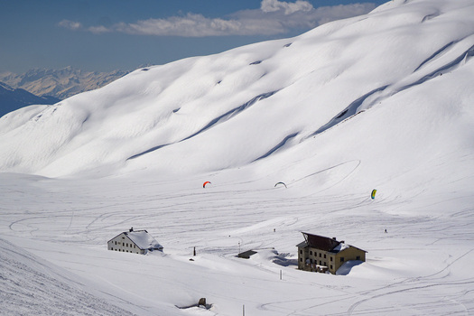 Aerial view of Colle del Piccolo San Bernardo with snow covered slopes mountain huts and snowkiters gliding over the white terrain under a clear blue sky in La Thuile Valle d Aosta Italy. Aerial view of Colle del Piccolo San Bernardo with snow covered slopes mountain huts and snowkiters gliding over the white terrain under a clear blue sky in La Thuile Valle d Aosta Italy.