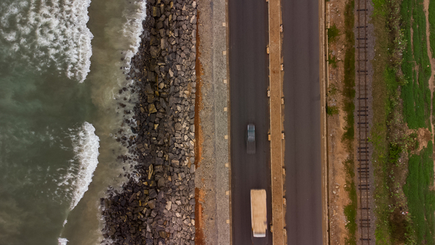 Aerial view of the Accra Tema Beach Road running along the rocky coastline with ocean waves adjacent railway tracks and vehicles on the asphalt road in Accra Greater Accra Region Ghana.