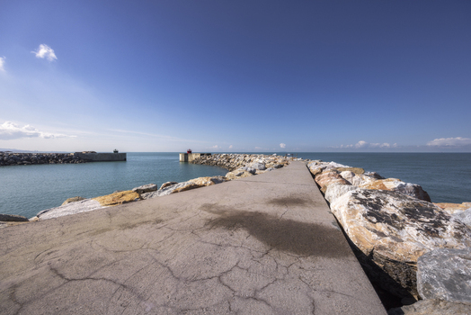 View of the concrete breakwater and large protective rocks leading into the calm blue sea under a clear sky Marina di Pisa Tuscany Italy.