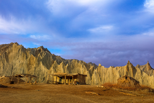 View of traditional mud huts set against the dramatic eroded rock formations of Hingol National Park under a cloudy sky in Awaran Balochistan Pakistan.