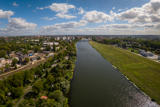 Aerial view of the Oder River flowing through Opole with green banks urban infrastructure and the historic old town in the distance under a bright sky. Opole Opole Voivodeship Poland.