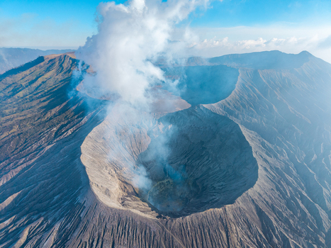 Aerial view of Mount Bromo crater with volcanic smoke rising from the caldera surrounded by rugged volcanic landscape Tosari East Java Indonesia.