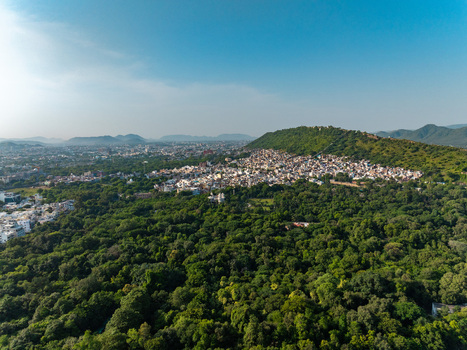 Aerial view of the historic city nestled among lush green hills and dense forests in Udaipur Rajasthan India.