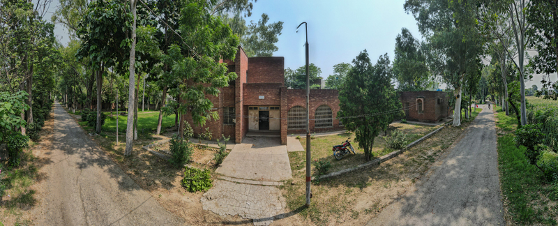 Lahore Pakistan 08 September 2026 Aerial view of the Fisheries Complex in Manawan featuring brick buildings lush trees dirt paths and a motorcycle under a clear blue sky.