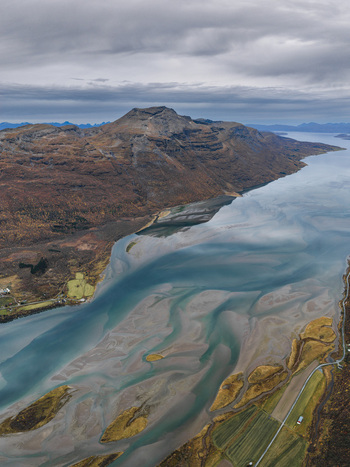 Aerial view of the rugged landscape of Senja island featuring tidal flats winding waterways autumn colored mountains and overcast sky in Senja Troms Norway.