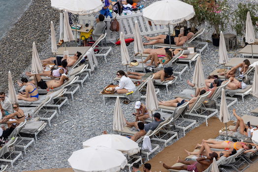 Aerial view of people relaxing on lounge chairs under white umbrellas at a pebble beach club in Nice Provence Alpes Cote d Azur France. Aerial view of people relaxing on lounge chairs under white umbrellas at a pebble beach club in Nice Provence Alpes Cote d Azur France.