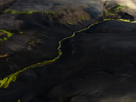 Aerial view of a vibrant green river snaking through a stark black volcanic landscape contrasting textures under a soft light Iceland. Aerial view of a vibrant green river snaking through a stark black volcanic landscape contrasting textures under a soft light Iceland.