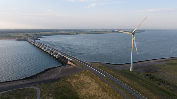 Aerial view of the Eastern Scheldt Storm Surge Barrier with a large wind turbine standing on the coast in Vrouwenpolder Zeeland Netherlands. Aerial view of the Eastern Scheldt Storm Surge Barrier with a large wind turbine standing on the coast in Vrouwenpolder Zeeland Netherlands.