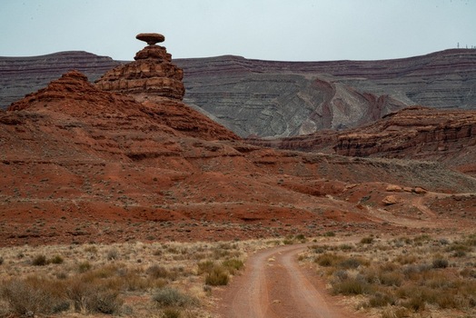 View of the iconic Mexican Hat Rock formation rising above the red desert landscape with a dirt road leading towards the sandstone cliffs in Oljato Monument Valley Utah United States.