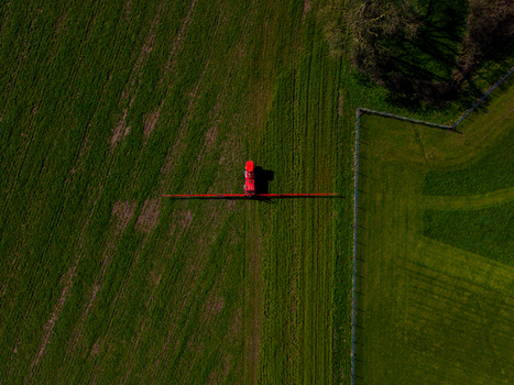 Aerial view of a red tractor spraying a green field in the rural landscape of Gnosall Heath Gnosall England United Kingdom. Aerial view of a red tractor spraying a green field in the rural landscape of Gnosall Heath Gnosall England United Kingdom.