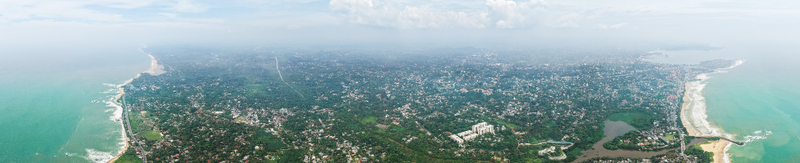 Aerial view of the sprawling coastal cityscape with dense tropical vegetation and waves crashing along the shoreline in Galle Southern Province Sri Lanka. Aerial view of the sprawling coastal cityscape with dense tropical vegetation and waves crashing along the shoreline in Galle Southern Province Sri Lanka.