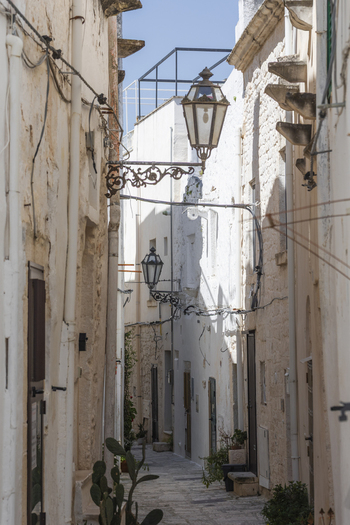 View of a narrow alleyway with white washed stone walls vintage street lamps and a prickly pear cactus in Ostuni Apulia Italy. View of a narrow alleyway with white washed stone walls vintage street lamps and a prickly pear cactus in Ostuni Apulia Italy.
