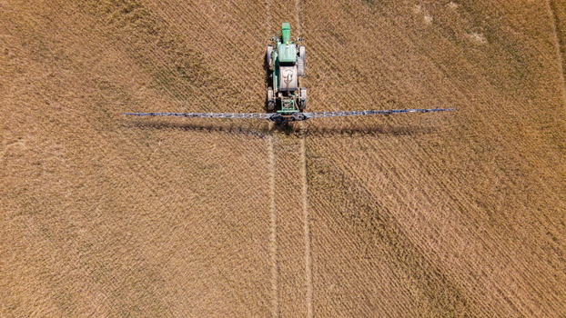 Aerial view of a green tractor spraying a large golden wheat field with long boom arms creating distinct tire tracks in the soil in Philadelphia Western Cape South Africa. Aerial view of a green tractor spraying a large golden wheat field with long boom arms creating distinct tire tracks in the soil in Philadelphia Western Cape South Africa.