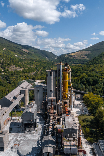Aerial view of Sacci S.P.A. cement factory with silos and industrial structures nestled in a valley surrounded by green hills in Castelraimondo Marche Italy. Aerial view of Sacci S.P.A. cement factory with silos and industrial structures nestled in a valley surrounded by green hills in Castelraimondo Marche Italy.
