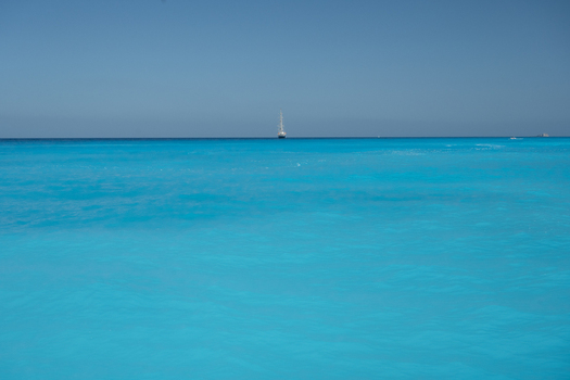 View of a sailboat sailing on the bright turquoise waters of the Ionian Sea under a clear blue sky in Lefkada Greece.