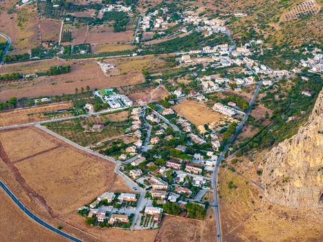 Aerial view of a village nestled at the base of a rocky cliff with surrounding agricultural fields winding roads and Mediterranean vegetation in Palermo Sicily Italy. Aerial view of a village nestled at the base of a rocky cliff with surrounding agricultural fields winding roads and Mediterranean vegetation in Palermo Sicily Italy.