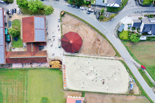 Aerial view of Reitclub In der Point Poxdorf featuring stables an outdoor riding arena and solar panels on rooftops in Poxdorf Bayern Germany. Aerial view of Reitclub In der Point Poxdorf featuring stables an outdoor riding arena and solar panels on rooftops in Poxdorf Bayern Germany.