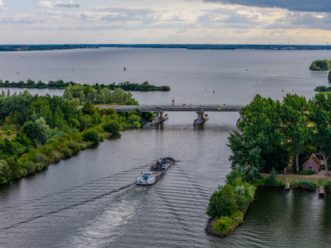 Aerial view of a barge navigating the waterway near Harderhaven with a bridge lush green trees and the expansive Wolderwijd lake in Zeewolde Flevoland Netherlands.
