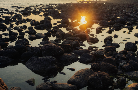 View of sunbursts kiss the wet rocks along the tranquil shore mirroring the golden sky above creating a serene coastal scene Chiplun Maharashtra India. View of sunbursts kiss the wet rocks along the tranquil shore mirroring the golden sky above creating a serene coastal scene Chiplun Maharashtra India.