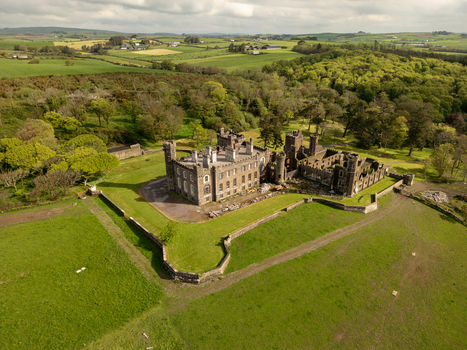 Aerial view of Castlefreke Castle surrounded by lush green fields dense woodland and rolling countryside in Castlefreke County Cork Ireland.