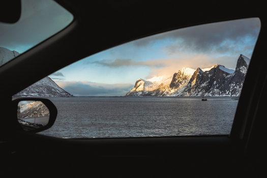 View of the sea meeting snow capped mountains under a cloudy sky framed by the dark interior of a car capturing the essence of a journey Indregård Troms Norway. View of the sea meeting snow capped mountains under a cloudy sky framed by the dark interior of a car capturing the essence of a journey Indregård Troms Norway.