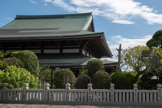 View of a traditional Japanese temple with a green roof and intricate architectural details framed by lush greenery and a stone fence Narita Chiba Japan. View of a traditional Japanese temple with a green roof and intricate architectural details framed by lush greenery and a stone fence Narita Chiba Japan.
