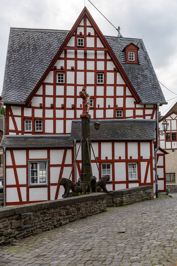 View of a historic half timbered house and a stone bridge featuring a crucifix monument with lion statues in Monreal Rhineland Palatinate Germany. View of a historic half timbered house and a stone bridge featuring a crucifix monument with lion statues in Monreal Rhineland Palatinate Germany.