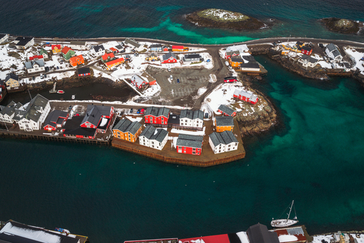 Aerial view of vibrant red and yellow buildings stand out against the snowy landscape and turquoise waters of Henningsv&aelig;r Nordland Norway.