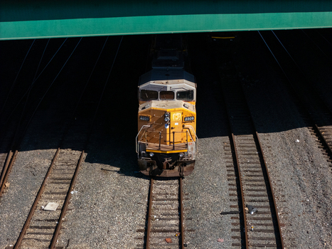 Aerial view of a yellow locomotive traveling on train tracks under a bridge in Carson California United States.