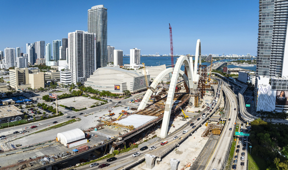 Aerial view of the signature arches of a bridge under construction contrasting against the modern skyline and Biscayne Bay Miami Florida USA. Aerial view of the signature arches of a bridge under construction contrasting against the modern skyline and Biscayne Bay Miami Florida USA.