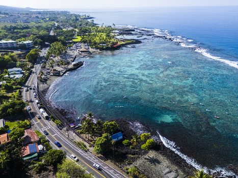 Aerial view of Kahalu u Beach Park featuring turquoise waters coral reefs and a coastal road lined with palm trees and volcanic rocks in Kailua Kona Hawaii United States. Aerial view of Kahalu u Beach Park featuring turquoise waters coral reefs and a coastal road lined with palm trees and volcanic rocks in Kailua Kona Hawaii United States.