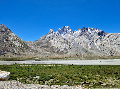 View of Penzi La road surrounded by snow capped Himalayan peaks rocky slopes and a green meadow under a clear blue sky Zanskar Ladakh India.