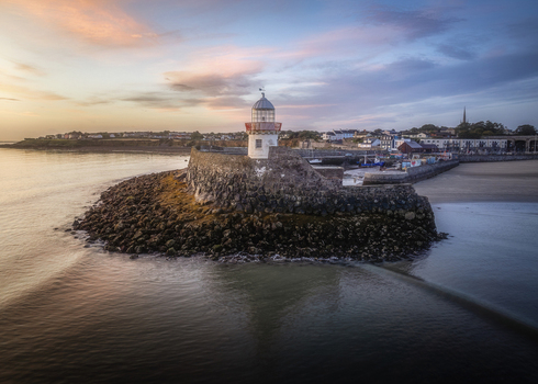 Aerial view of Balbriggan Harbour lighthouse situated on a stone breakwater with the coastal town and sunset sky in the background in Balbriggan County Dublin Ireland. Aerial view of Balbriggan Harbour lighthouse situated on a stone breakwater with the coastal town and sunset sky in the background in Balbriggan County Dublin Ireland.
