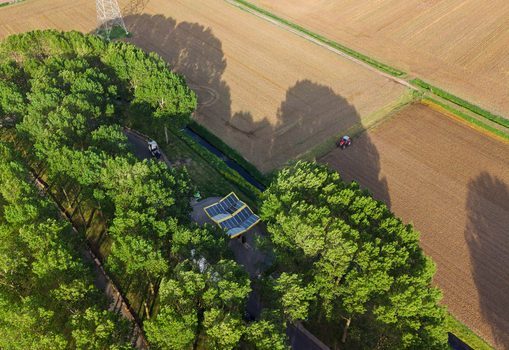 Aerial view of the Fastned Charging Station with its solar panel roof surrounded by lush green trees and agricultural fields in Vierpolders Zuid Holland Netherlands. Aerial view of the Fastned Charging Station with its solar panel roof surrounded by lush green trees and agricultural fields in Vierpolders Zuid Holland Netherlands.