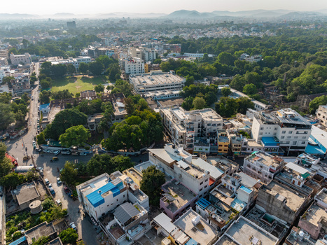 Aerial view of the dense urban landscape of Udaipur featuring residential buildings lush green trees and winding streets in Udaipur Rajasthan India.